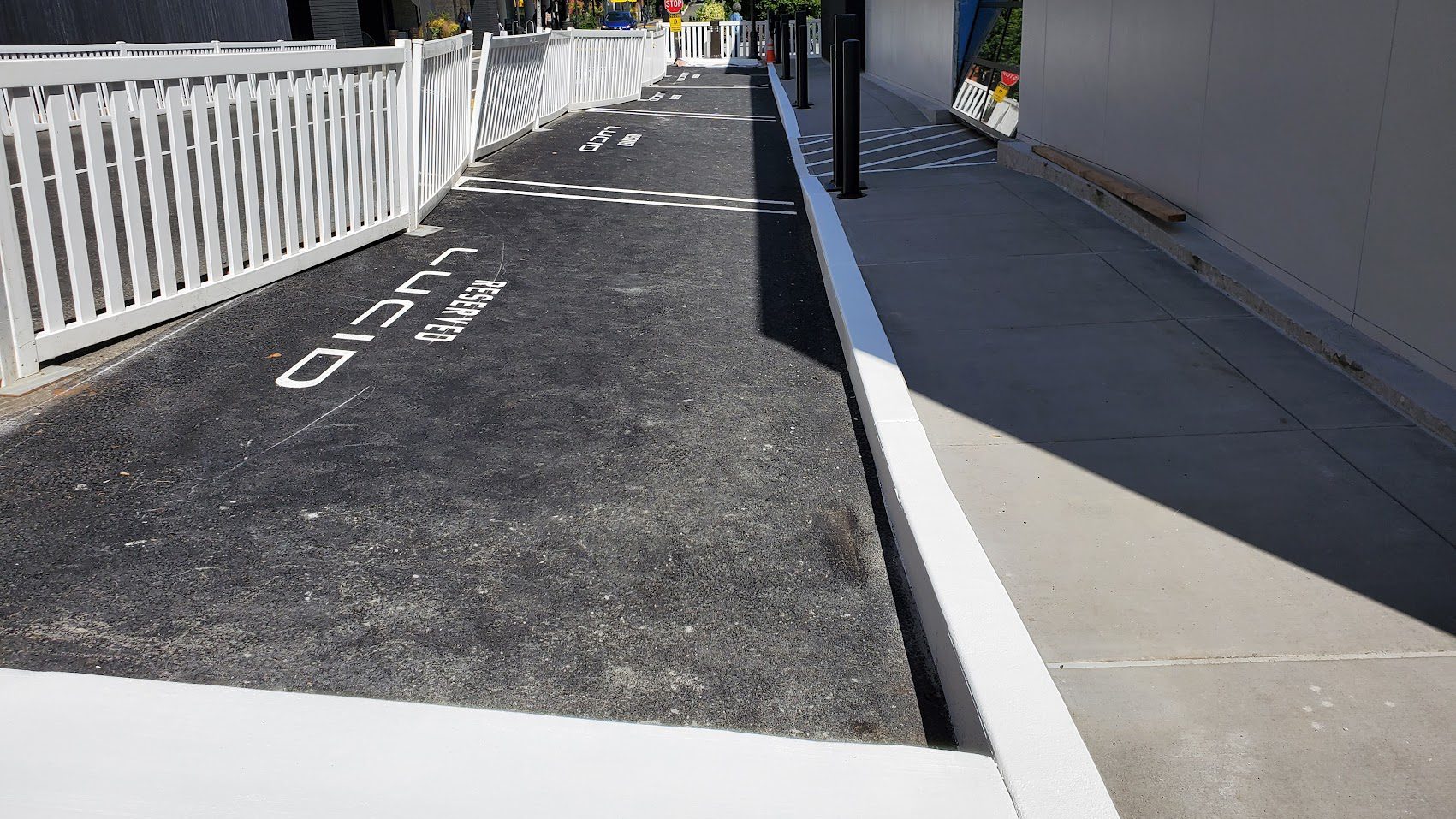 Newly paved bike lane next to sidewalk with white curb and railing.