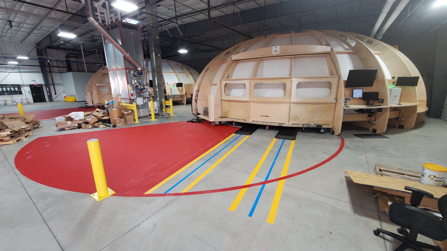 Large wooden structure in a warehouse with colored tape on the floor.