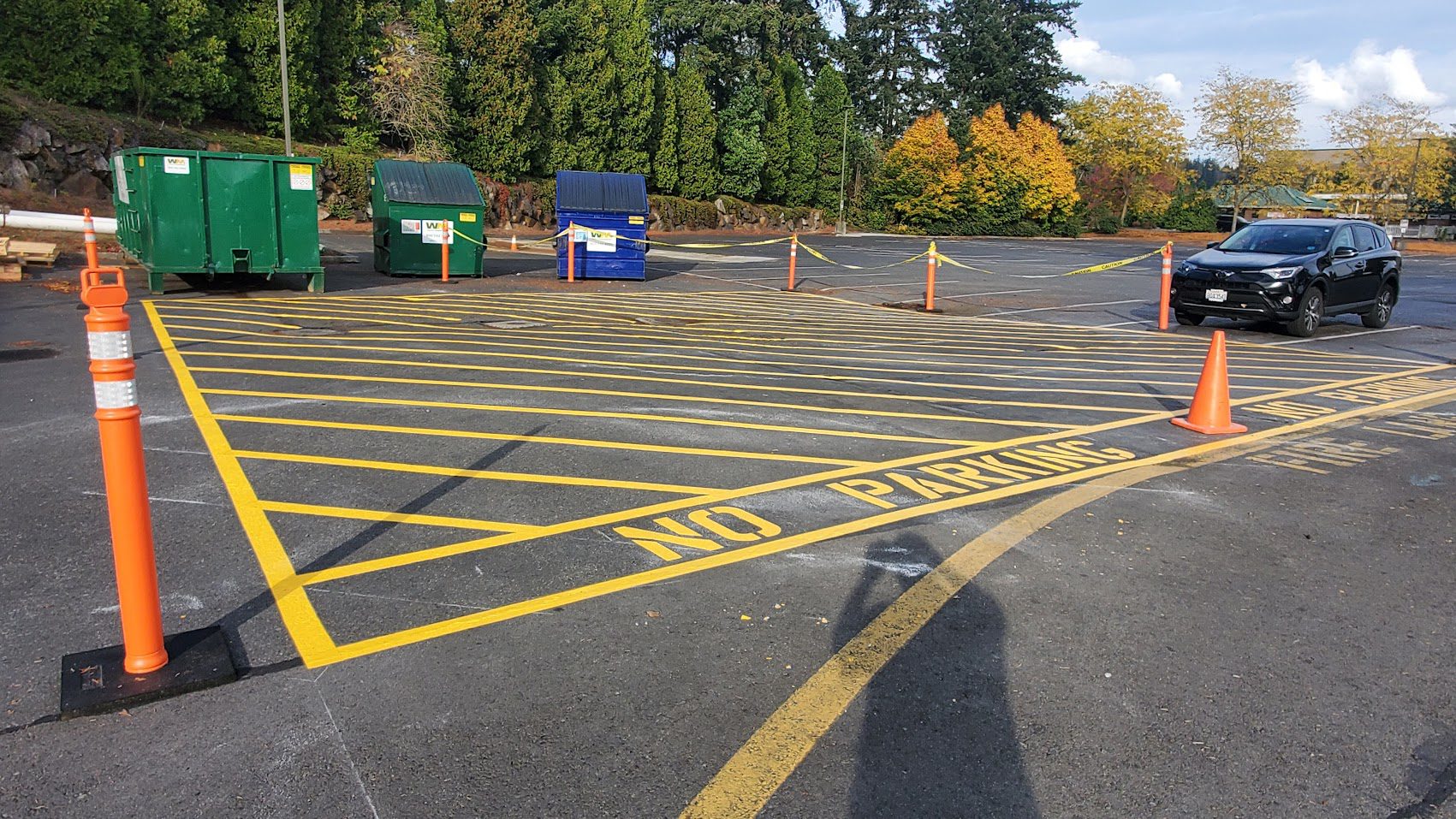 Empty parking lot with yellow no parking markings and dumpsters in the background.