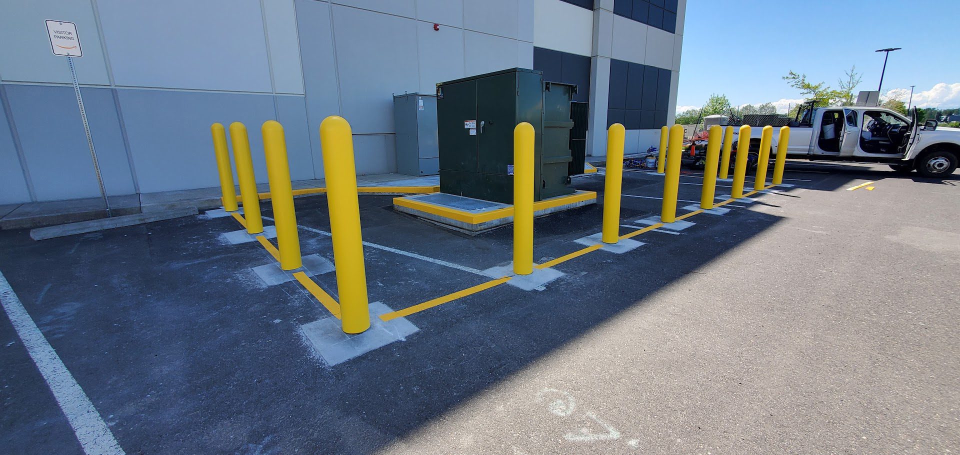 Yellow bollards protecting electrical equipment in a parking lot.