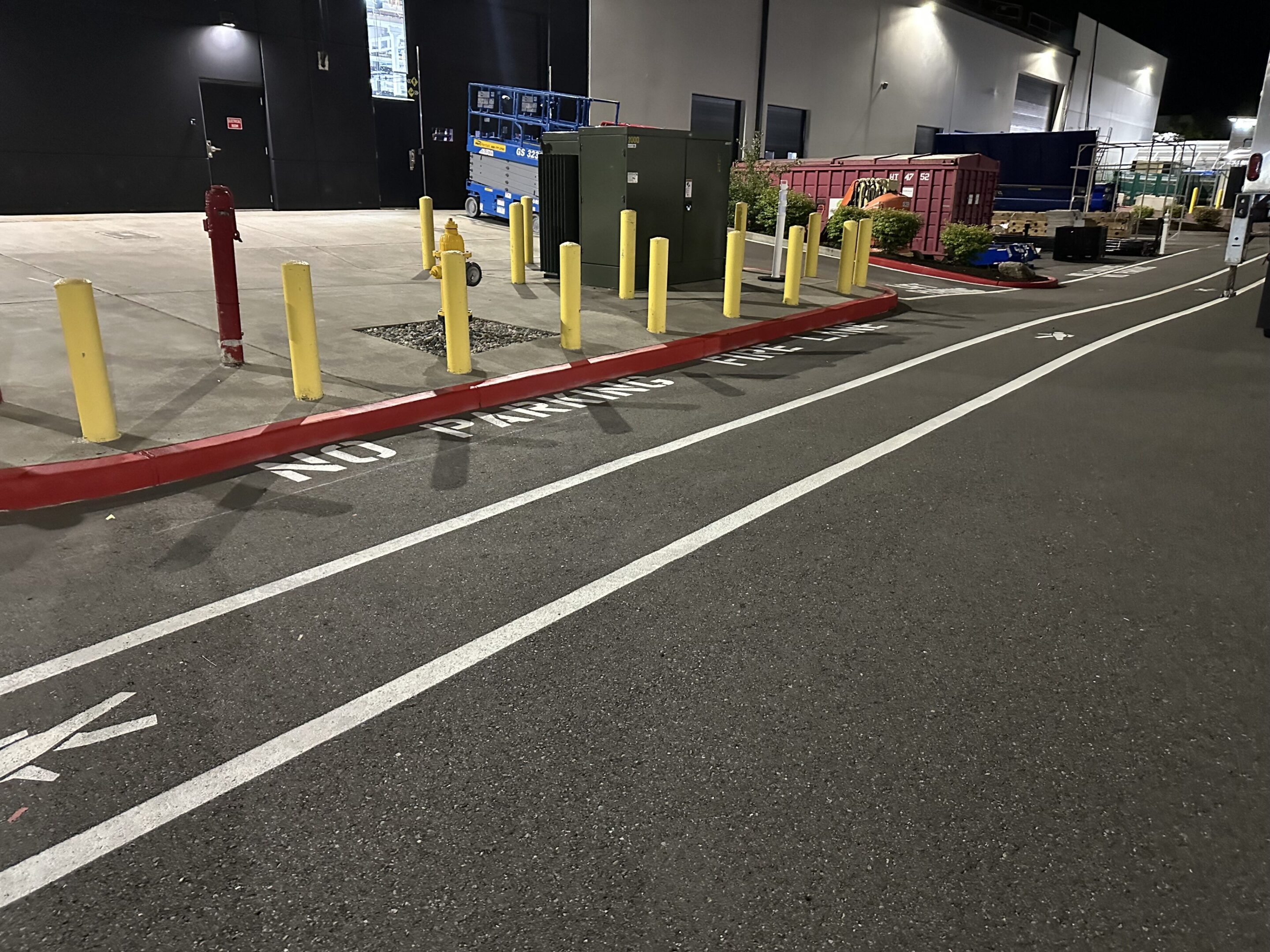 Parking lot with yellow bollards and a red curb at night.