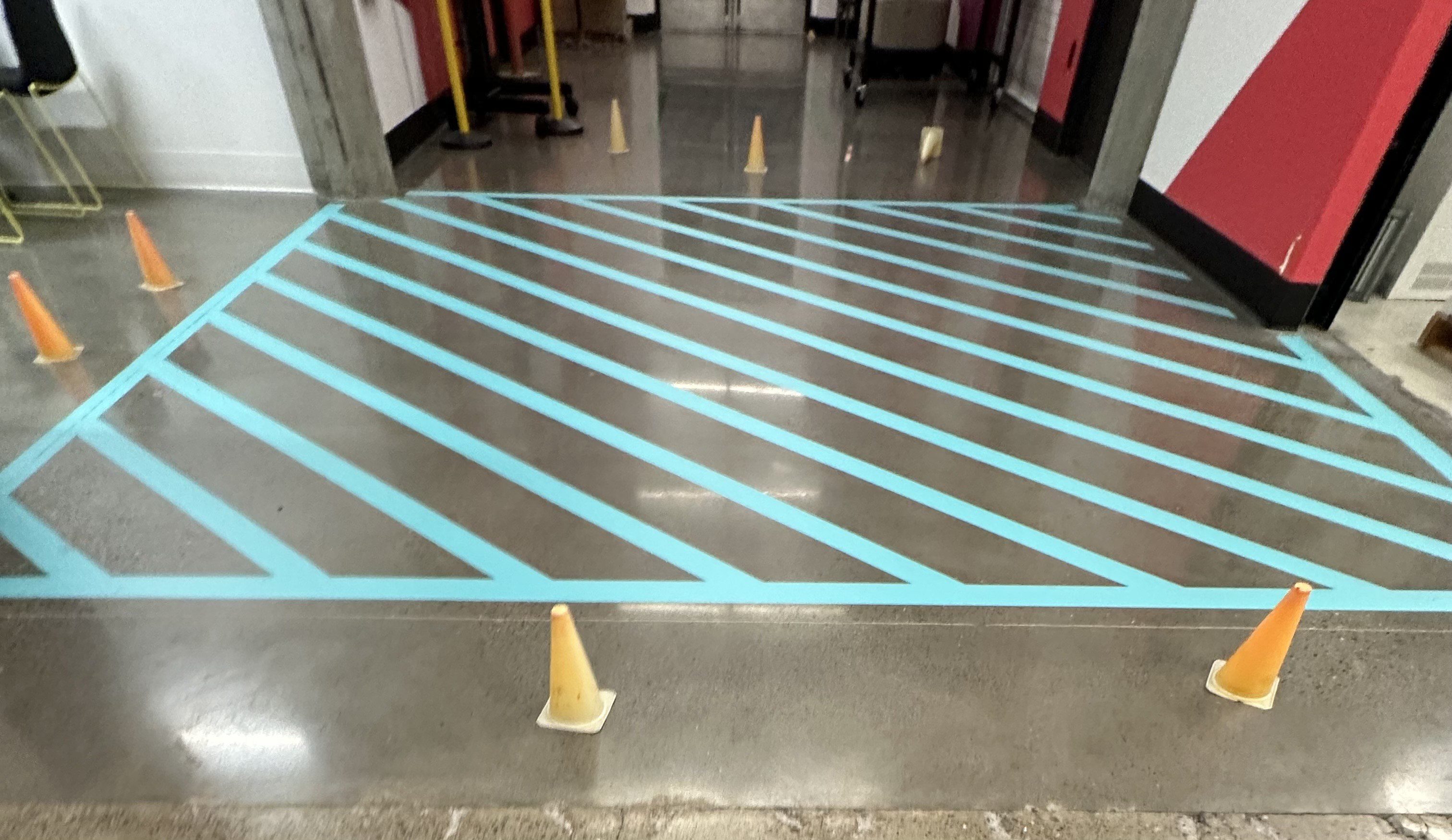 Blue diagonal stripes painted on a floor with yellow cones around.