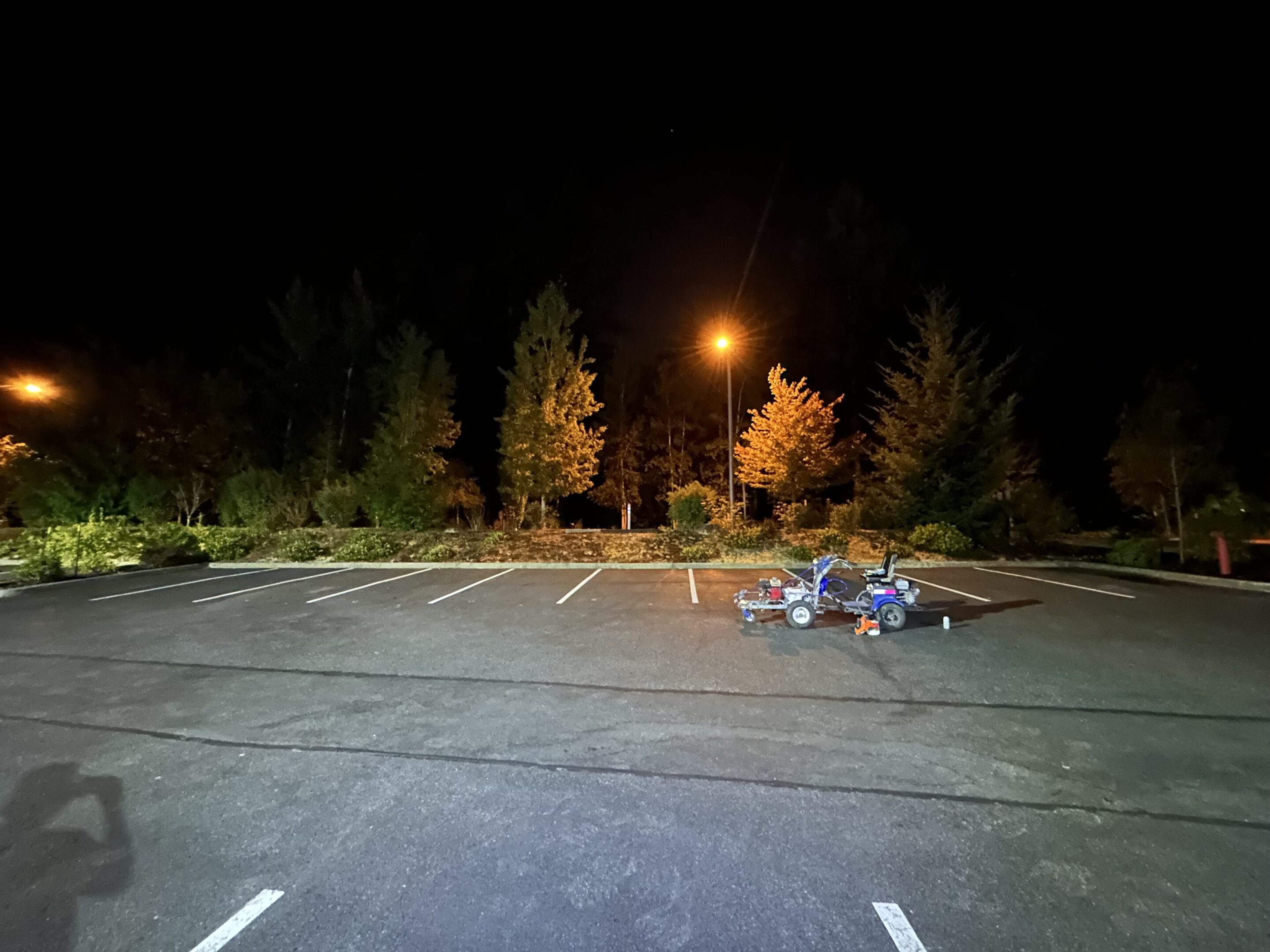 A group of people sitting in an empty parking lot at night under streetlights.