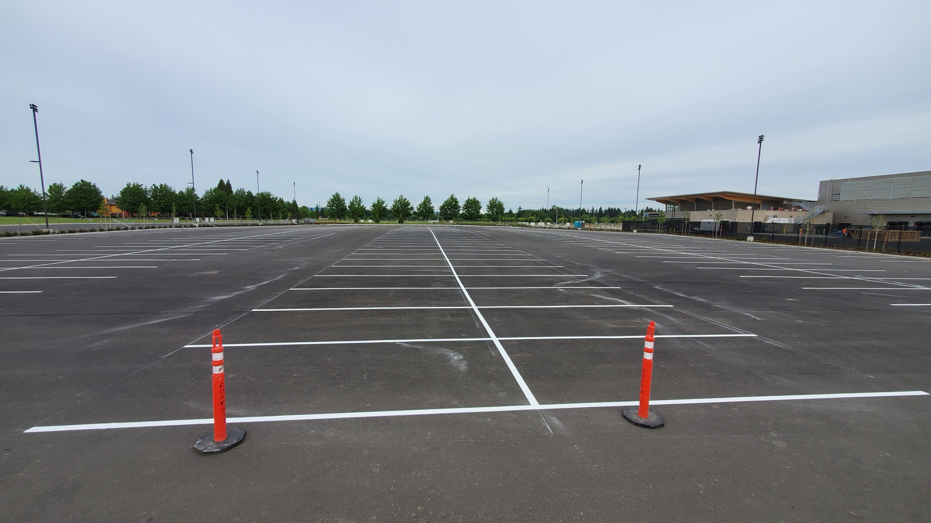Empty parking lot with marked spaces and orange bollards under a cloudy sky.
